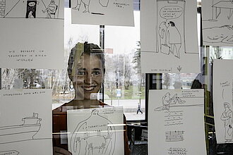 Die Illustratorin Johanna Benz hinter einer Glasscheibe, an der Zeichnungen von ihr kleben (Foto: Jörg Farys)
